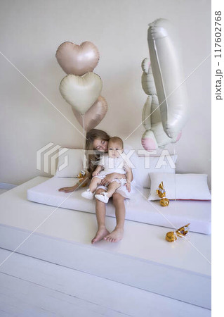 a        photo session on the first birthday of a baby girl with her  teenage sister, in pastel colors, minimalism 117602768