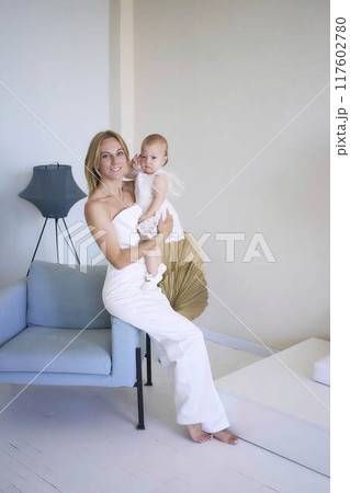 mother with a baby girl in a stylish white minimalist interior in white clothes 117602780