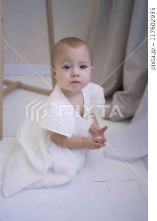 a baby girl in a white dress on the floor near the mirror a baby girl in a white dress on the floor near the mirror 117602935