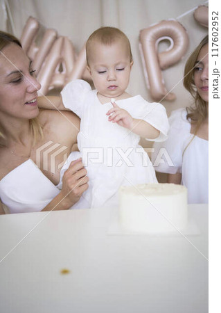 baby girl tries her first birthday cake with mom and pre-teen sister 117602952