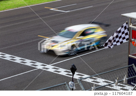 Race car crossing finish line on track and pass checkered race flag, Checkered racing finish flag with Race car crossing the finish line on circuit. 117604187