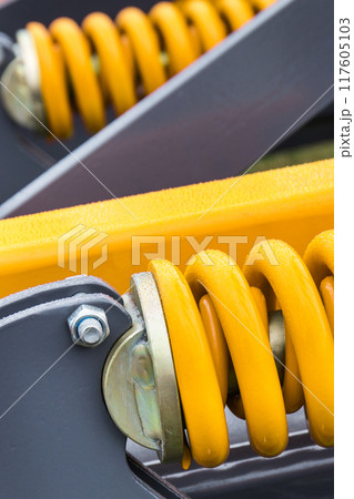Yellow hard spring made of steel. Part of big industrial or agricultural machine 117605103