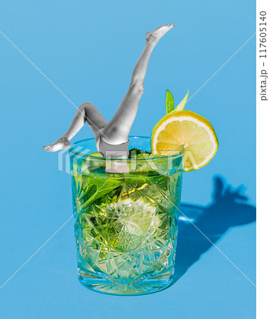 Poster. Contemporary art collage. Legs in mid-dive emerge from refreshing glass of Mojito, with slice of lemon perched on rim. Poster. Contemporary art collage. Legs in mid-dive emerge from refreshing glass of Mojito, with slice of lemon perched on rim. 117605140