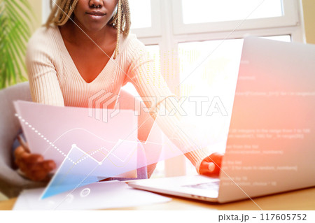 A woman is sitting at a desk with a laptop and a stack of papers A woman is sitting at a desk with a laptop and a stack of papers 117605752