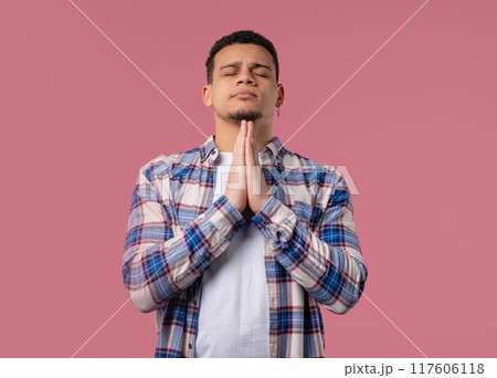 Young multiracial man praying with crossed fingers on pink. Guy begs someone 117606118