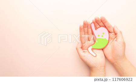 Human hands holding stomach with gastric acid made from paper. Gastroesophageal reflux disease (GERD) or acid reflux symptoms. Gastrointestinal system disease and digestive problems. Human hands holding stomach with gastric acid made from paper. Gastroesophageal reflux disease (GERD) or acid reflux symptoms. Gastrointestinal system disease and digestive problems. 117606922