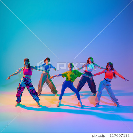 Dancers, girls deliver performance full of emotion and power in neon light against gradient studio background. Dancers, girls deliver performance full of emotion and power in neon light against gradient studio background. 117607152