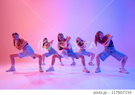 Teenagers, girls dressed casual attire dancing hip-hop in neon light against gradient pink background. Rhythm and energy. Teenagers, girls dressed casual attire dancing hip-hop in neon light against gradient pink background. Rhythm and energy. 117607156