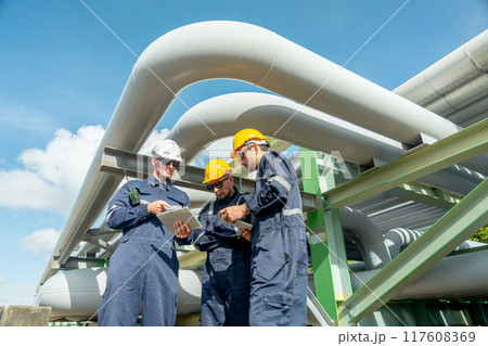 Group of engineer or factory technician worker team stand near and under petrochemical gas pipeline and use tablet to discuss about their work in workplace. Group of engineer or factory technician worker team stand near and under petrochemical gas pipeline and use tablet to discuss about their work in workplace. 117608369