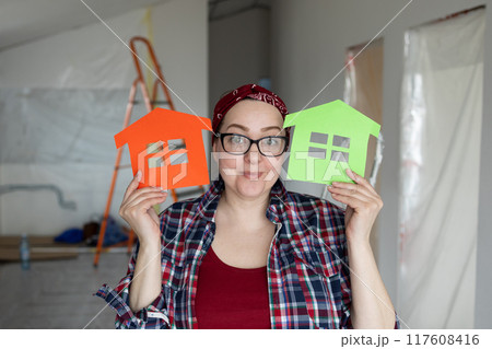 A Creative Woman Enthusiastically Holding Colorful House Cutouts in a Bright Renovation Space 117608416