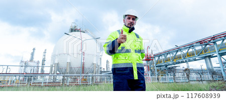 Portrait of engineer or technician worker stand with hold walkie-talkie and show thumbs up in front of petrochemical tank also look to right side. Portrait of engineer or technician worker stand with hold walkie-talkie and show thumbs up in front of petrochemical tank also look to right side. 117608939
