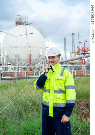 Vertical image of engineer or technician worker stand with hold walkie-talkie in front of petrochemical tank with day light. 117608944