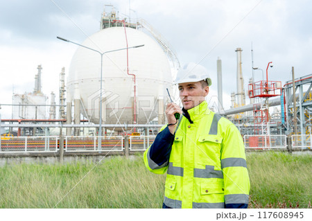 Factory engineer or technician worker man hold walkie-talkie to discuss with coworker and stand in front of tank of refining and petrochemical factory with day light. Factory engineer or technician worker man hold walkie-talkie to discuss with coworker and stand in front of tank of refining and petrochemical factory with day light. 117608945