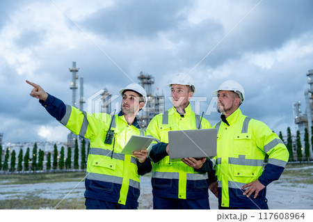Group of engineer or technician workers stand in front of petrochemical factory and use laptop to discuss their work with one point to left side. Group of engineer or technician workers stand in front of petrochemical factory and use laptop to discuss their work with one point to left side. 117608964