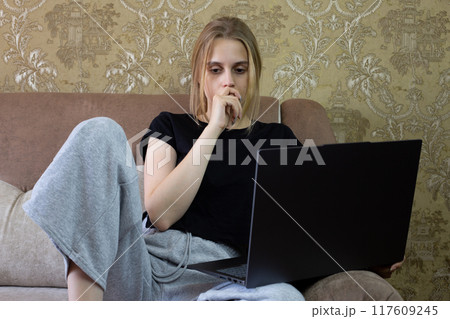 Thoughtful young woman is deeply and intently engaged in her productive work on her laptop while comfortably sitting on sofa Thoughtful young woman is deeply and intently engaged in her productive work on her laptop while comfortably sitting on sofa 117609245