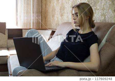 Young woman is focused on her laptop while relaxing at home, highlighting remote work and comfort Young woman is focused on her laptop while relaxing at home, highlighting remote work and comfort 117609248