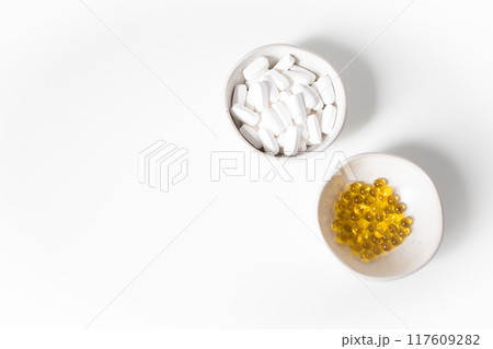 White and yellow pills in small bowls on a white background 117609282