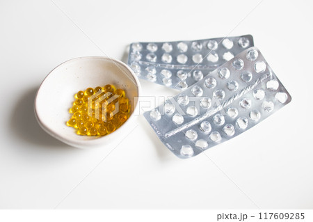 Yellow pills in small bowl and empty blisters on a white background 117609285