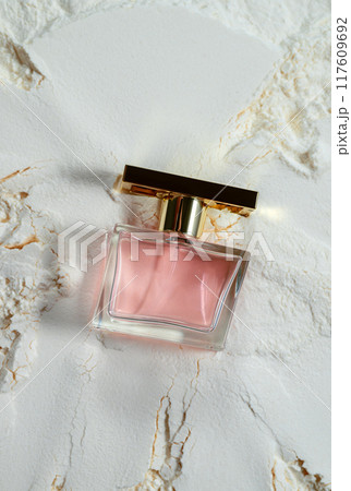 An elegant perfume bottle with a pink liquid, captured on a textured, cracked white surface 117609692