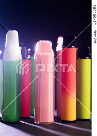 A set of colorful disposable electronic cigarettes of different shapes on a black background with smoke. Concept of modern smoking, vaping and nicotine. 117609693