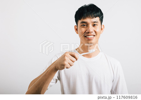 Portrait of a happy Thai man confidently brushing his teeth for dental health. Studio shot isolated on white, promoting oral hygiene and a bright smile. 117609816