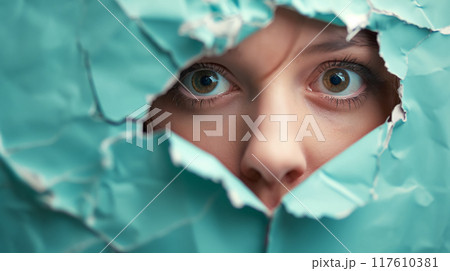Eyes peering through a torn turquoise paper. 117610381