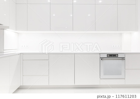 Front view of a modern luxury trendy snow white kitchen with many cabinets Front view of a modern luxury trendy snow white kitchen with many cabinets 117611203