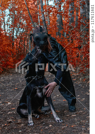 a girl in a bdsm costume and a black mask and with a dog in red forest.an an idea for Halloween. 117611681