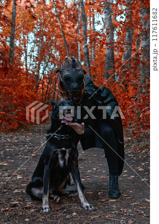 a girl in a bdsm costume and a black mask and with a dog in red forest.an an idea for Halloween. 117611682