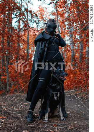 a girl in a bdsm costume and a black mask and with a dog in red forest.an an idea for Halloween. a girl in a bdsm costume and a black mask and with a dog in red forest.an an idea for Halloween. 117611683