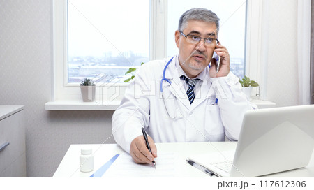 Male Doctor Talking on the Phone at His Desk 117612306