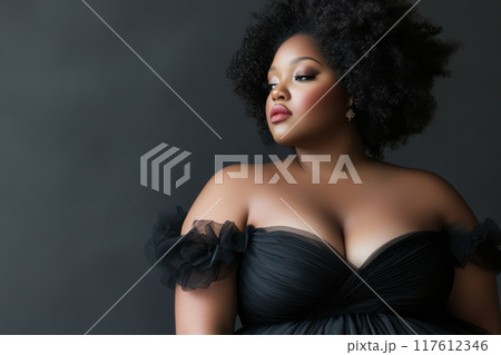 Elegant plus size woman with natural curly hair wearing a black dress 117612346
