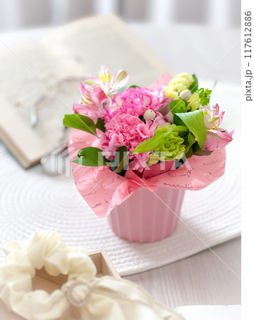 カーネーションを中心としたピンクの花束がテーブルに置かれた優しい雰囲気のフラワーアレンジメント 117612886