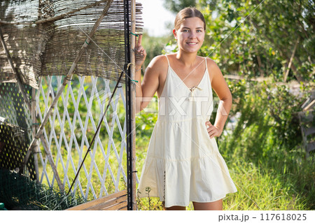 Female peasant girl stands near garden bed, near chicken coop and enjoys country activities 117618025