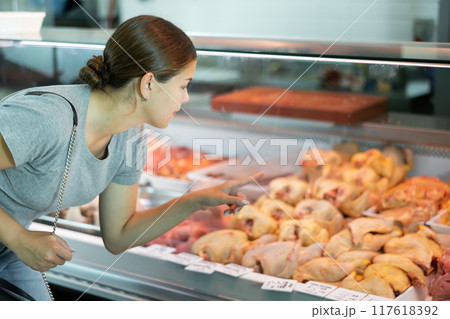 Young woman buyer chooses chicken in butcher shop 117618392