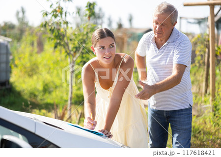 Courier girl fill out documents on hood of car in presence of senior man customer 117618421