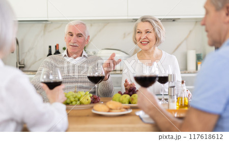 Two mature married couples are sitting at table, enjoying food and wine, chatting. 117618612