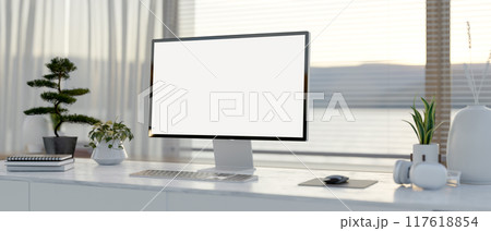 A computer desk featuring a computer with a white-screen mockup on a table in a modern white room. 117618854