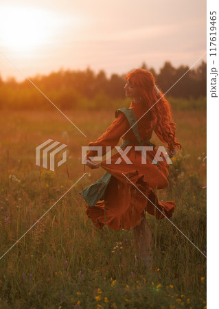 A shepherdess woman with red hair and a green dress sits in a field of flowers. 117619465