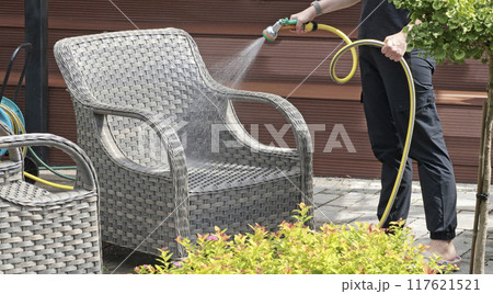 Anonymous cleaning, hose water washing wicker furniture from summer. Structures in backyard. Cleanliness and order.  117621521