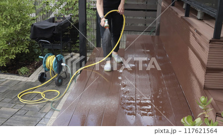 Anonymous cleaning, hose washing deck in summer. Structures in backyard. Clean and orderly.  117621564