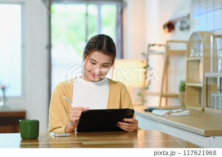 Young woman in casual clothes using digital tablet sitting in a modern kitchen Young woman in casual clothes using digital tablet sitting in a modern kitchen 117621968