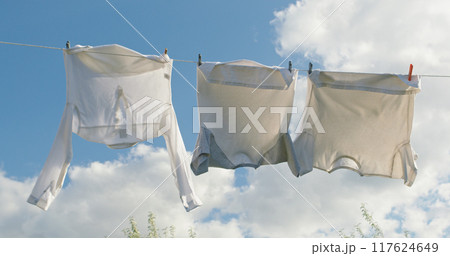 Three white shirts sway on a clothesline under a clear sky with soft clouds. Three white shirts sway on a clothesline under a clear sky with soft clouds. 117624649