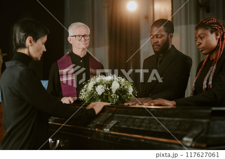 Black wooden coffin between biracial people who touching it in church 117627061