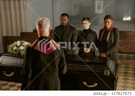 Biracial family and senior pastor standing next to black wooden coffin and saying goodbye to family member Biracial family and senior pastor standing next to black wooden coffin and saying goodbye to family member 117627075