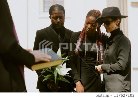African American young widow supported by her family while pastor reading prayer African American young widow supported by her family while pastor reading prayer 117627102