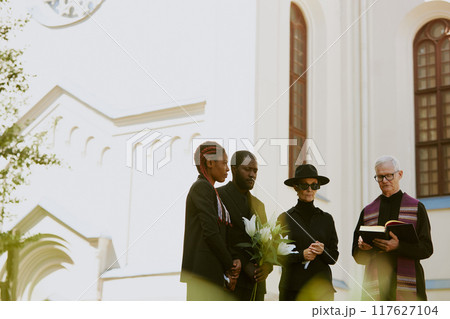 Biracial family mourning their bereavement at cemetery, senior pastor who reading prayer 117627104