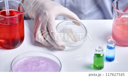 Scientist showing a hair sample in a petri dish. Laboratory concept with many glassware containing chemicals, powders and solutions Scientist showing a hair sample in a petri dish. Laboratory concept with many glassware containing chemicals, powders and solutions 117627585