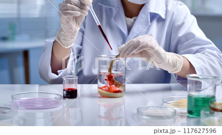 Close-up of each drop of red solution dropped by the scientist into the beaker containing the yellow damaged hair sample. Scene of hair research, experiments with hair samples 117627596