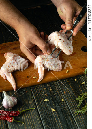 Chef cooking delicious chicken wings on kitchen table with spices and pepper. Fork in the cook hands. Concept of cooking delicious grill for lunch in restaurant Chef cooking delicious chicken wings on kitchen table with spices and pepper. Fork in the cook hands. Concept of cooking delicious grill for lunch in restaurant 117628236